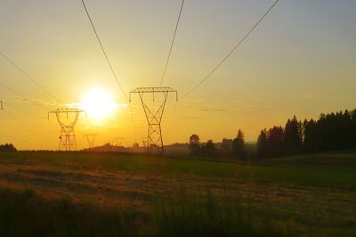 Silhouette electricity pylons on field against clear sky during sunset