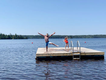 Man with arms raised on lake against clear sky