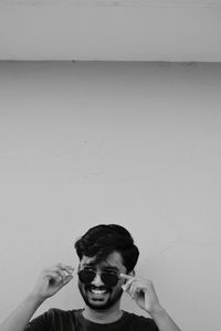 Portrait of young man holding camera against wall