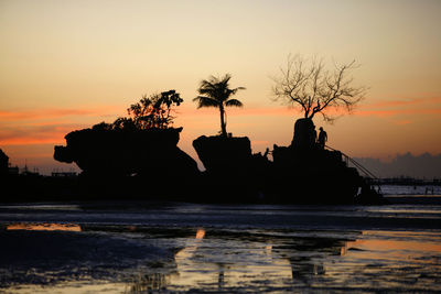 Silhouette rocks in sea against sky during sunset