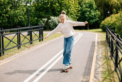 Cute blonde teenage girl is riding a skateboard in the city park.