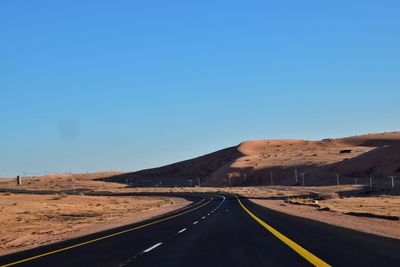 Road amidst desert against clear blue sky