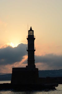 Low angle view of silhouette lighthouse against cloudy sky during sunset