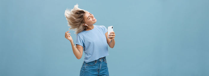 Rear view of woman holding smart phone against blue background