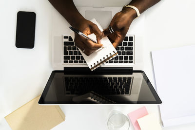 Woman with laptop writing in notepad while working on desk at office