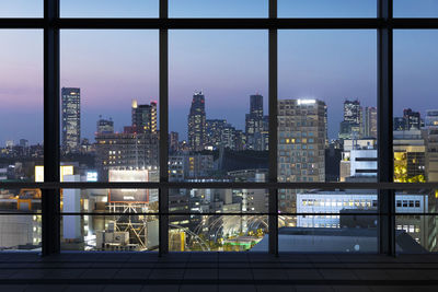 Illuminated buildings in city against sky seen through glass window