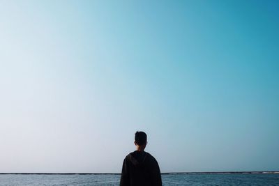 Rear view of man looking at sea against clear sky