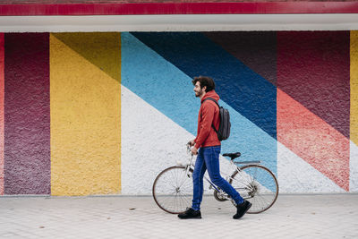 Man wheeling with bicycle on footpath in front of colorful wall