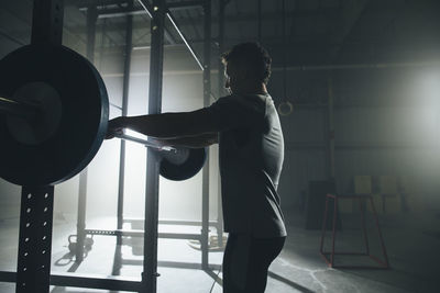 Side view of male athlete lifting barbell at gym