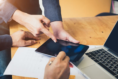 Cropped hands of colleagues discussing over digital tablet on desk in office