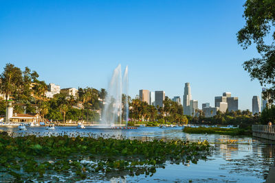 Fountain by lake and buildings against clear sky at echo park