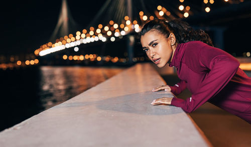Portrait of smiling woman sitting on illuminated bridge at night