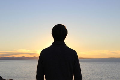 Rear view of silhouette man standing by sea against sky during sunset