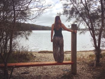 Rear view of woman standing by lake against sky