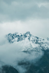 Scenic view of a snowcapped mountain surrounded by clouds against sky