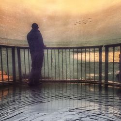 Silhouette man standing by railing against sea
