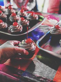 Cropped hand holding cupcake on table