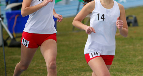 Two high school girls running in a track race on an outdoor track with a grass infield close up.