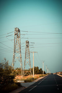 Electricity pylon by road against clear sky