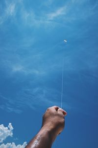 Cropped hand of man flying kite against blue sky