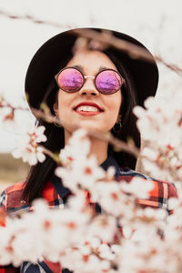 Portrait of woman wearing sunglasses and hat by pink flowers