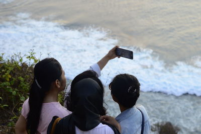 Friends taking selfie while standing against sea