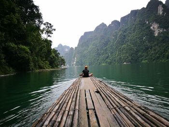 Man sitting on wooden raft at lake against sky