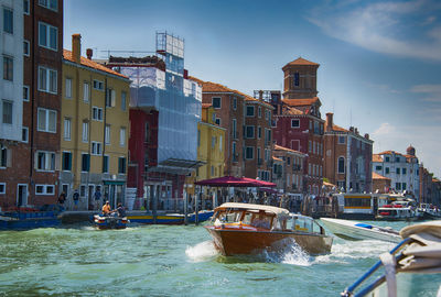 Boats in canal amidst buildings in city against sky