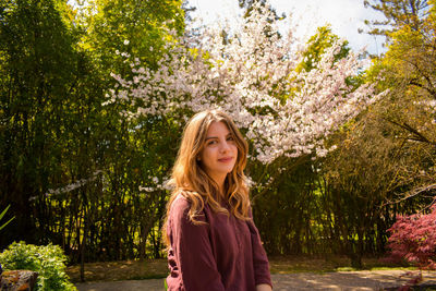 Portrait of beautiful woman standing against flowering tree in park