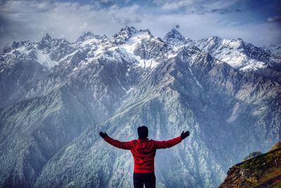 Rear view of man with arms outstretched standing on snowcapped mountain