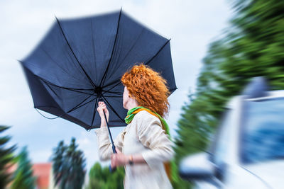 Blurred motion of woman holding umbrella against trees and sky