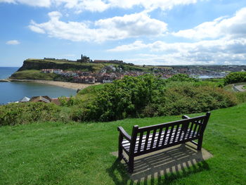 Empty bench on field against cloudy sky