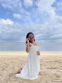 Young woman drinking water at beach against sky