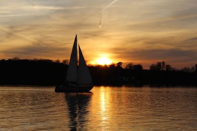 Silhouette sailboat on lake against sky during sunset