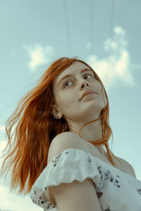 Low angle view of young woman looking away against sky