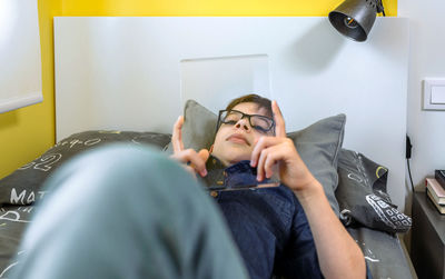 Relaxed boy holding futuristic transparent tablet laying over his bed