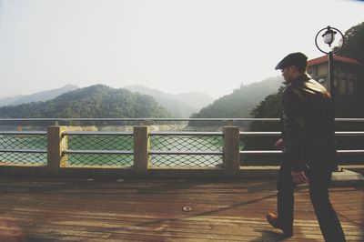 Rear view of man walking on wooden bridge against clear sky