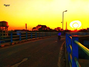 Rear view of man standing by railing against orange sky