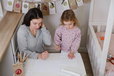Mother with toddler child writing christmas letter and doing advent calendar tasks in kids room