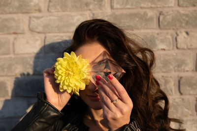 Portrait of woman holding flower against wall