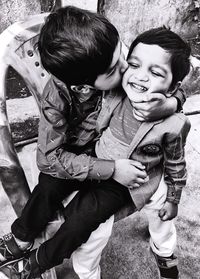 Boy kissing brother while sitting on chair outdoors