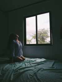 Rear view of woman sitting on bed at home