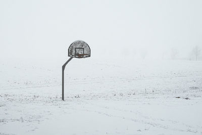 Basketball basket on snow covered field against sky