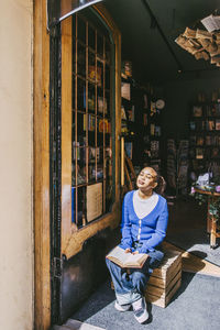 Young woman sitting in sunlight at entrance of bookstore