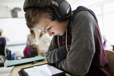 Side view of boy listening to headphones while using digital tablet in classroom
