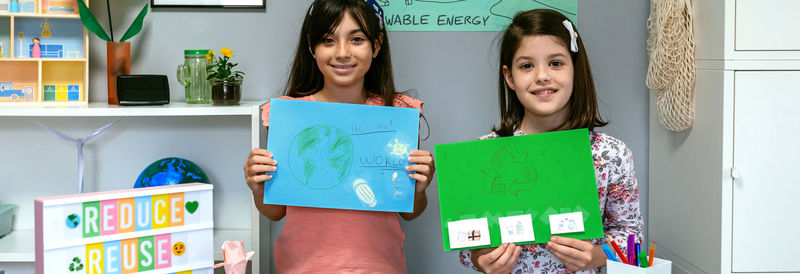 Female students looking at camera and showing drawings with ideas to be more ecological