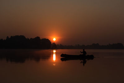 Silhouette man riding on lake against sky during sunset