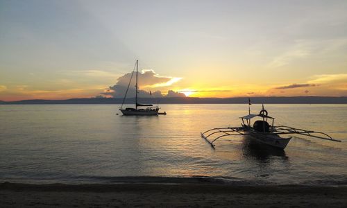 Silhouette sailboat in sea against sky during sunset