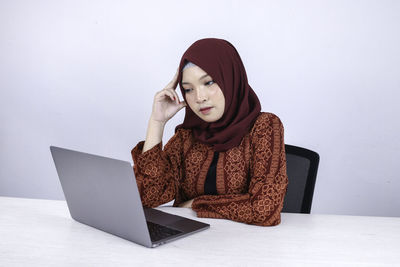 Young woman using phone while sitting on table against wall