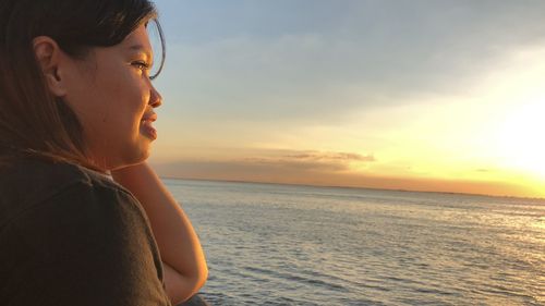 Side view of young woman looking away in sea against sky